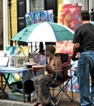 Artist Crystal A. Frascatore shelters under an umbrella during morning&nbsp;drizzle
